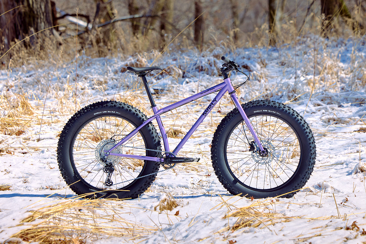 Surly Ice Cream Truck side view in purple color on a snowy landscape with dry grass and trees in the background